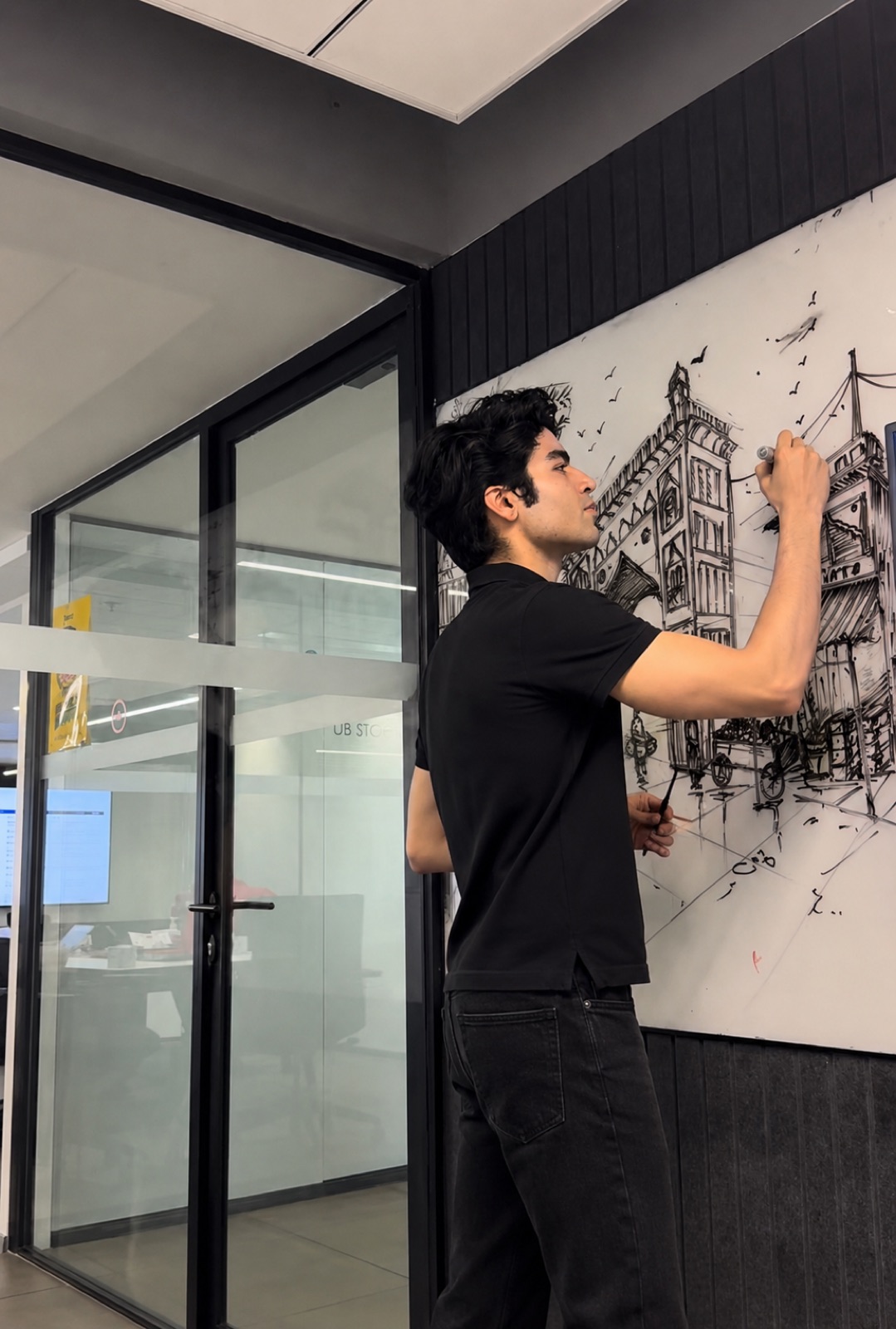 Dhairya Nagpal drawing a cityscape mural in marker on an office whiteboard